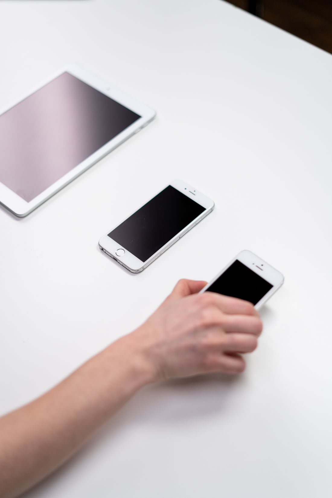 Ponsel dan tablet di atas meja putih dengan tangan hendak mengambil perangkat